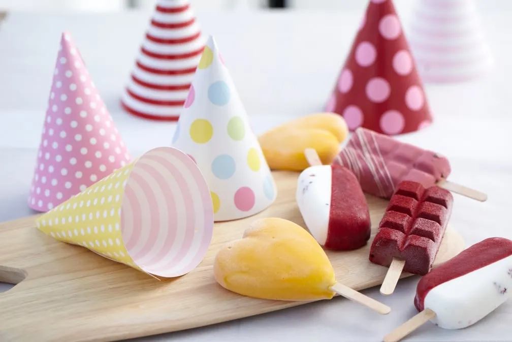 Gelato ice lollies on a wooden board with party hats